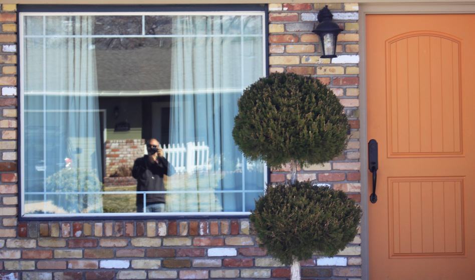 Reflection of Dominic Martinelli in window of brick house with orange door